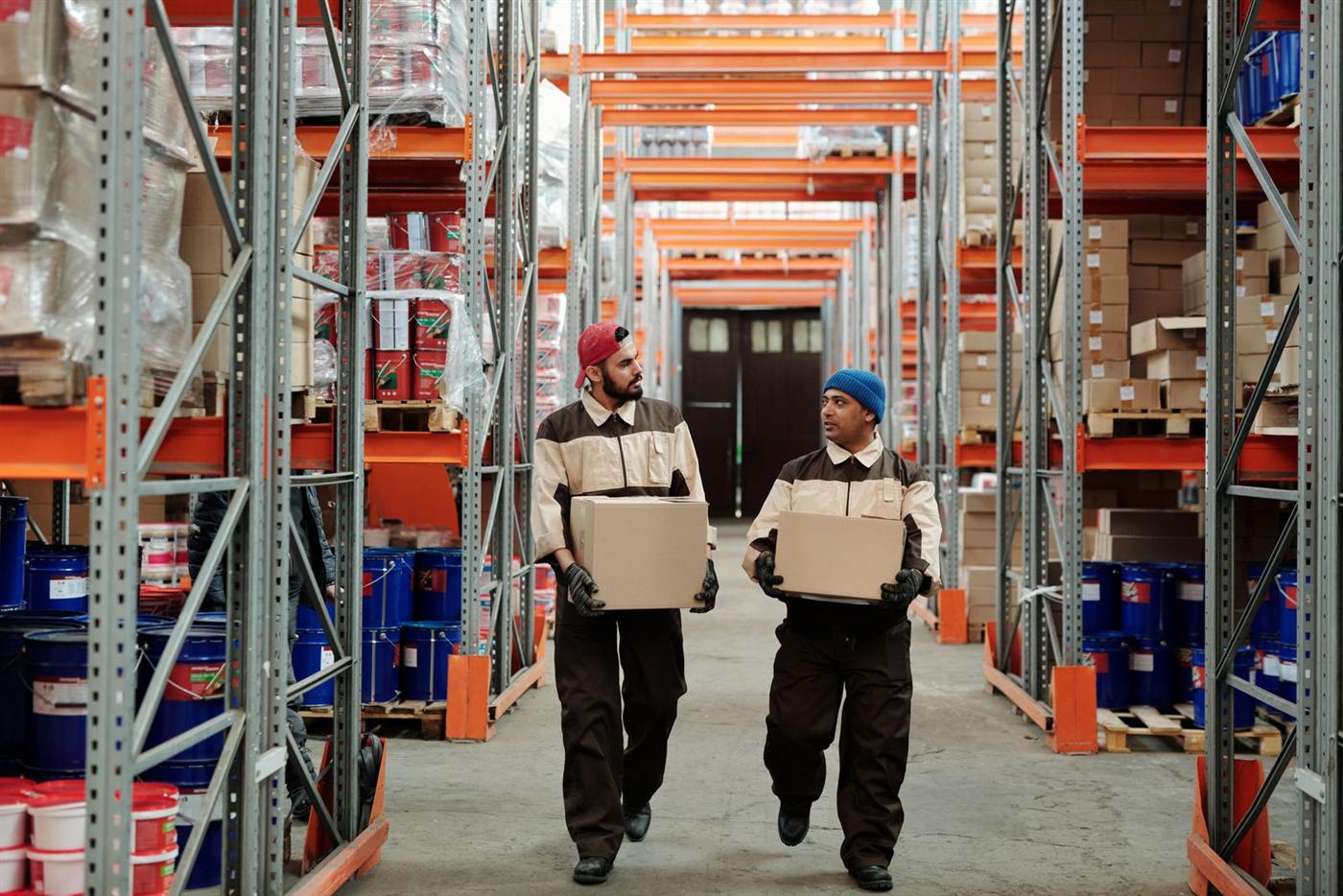 Two warehouse workers carrying boxes down an aisle